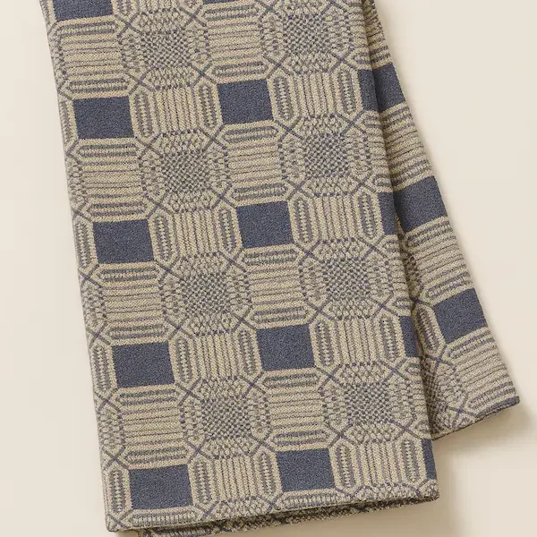 Angled folded Highland Manor Jacquard throw in navy and beige with intricate woven geometric pattern and four-side hem, displayed on a neutral beige background.