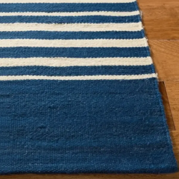 Corner detail of navy-and-ivory regatta stripe wool flatweave rug showing tight kilim weave and bound edge on wood floor