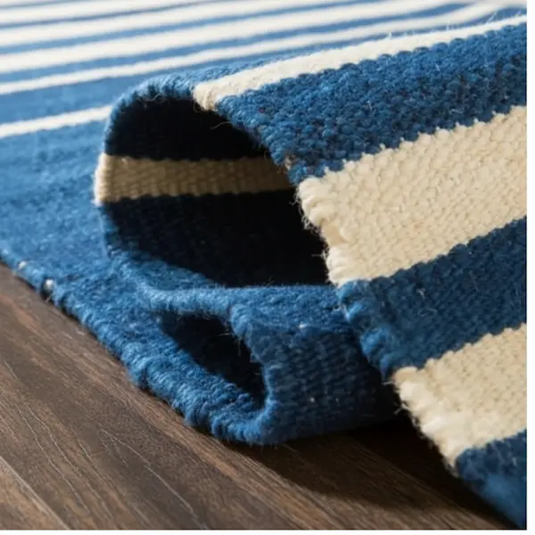 Rolled wool flatweave rug showing hand-stitched binding and underside of navy-and-ivory stripes on dark wood